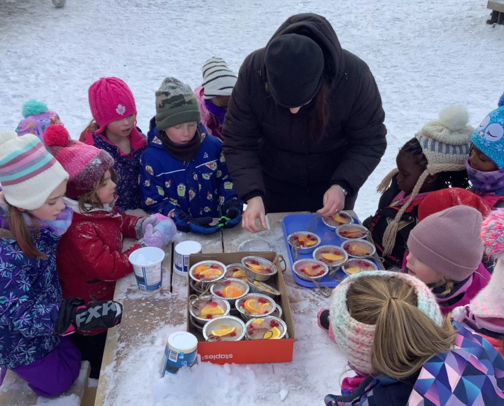 Teacher and group of Kindergarten students making frozen edible sun catcher bird feeders.
